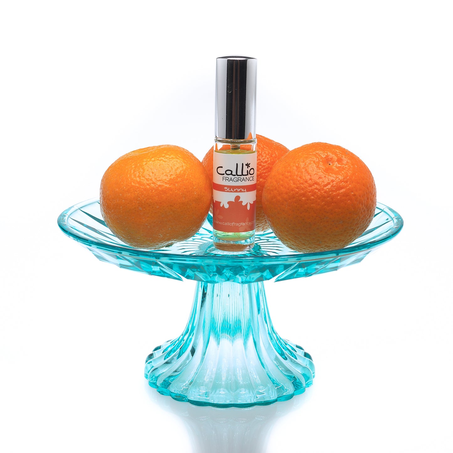 Image of a bottle of Sunny Travel-Size Perfume by Callio Fragranceon a teal pedestal, surrounded by mandarin oranges on a white background